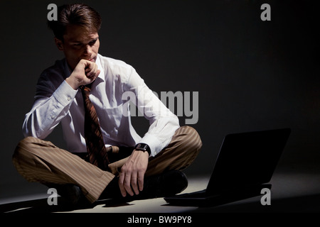 Image of man sitting on floor with laptop in front and looking at its monitor Stock Photo