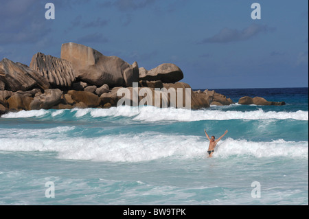 Man with arms up in the air standing in waves on Grand Anse, La Digue, Seychelles Stock Photo