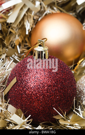 Red and gold Christmas baubles nestling in gold tinsel garland.  Vertical orientation. Stock Photo