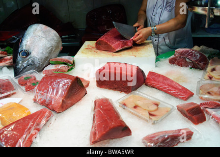 woman cuts a piece of fresh tuna fish with large knife at stall in La Boqueria market hall in Barcelona, Spain Stock Photo