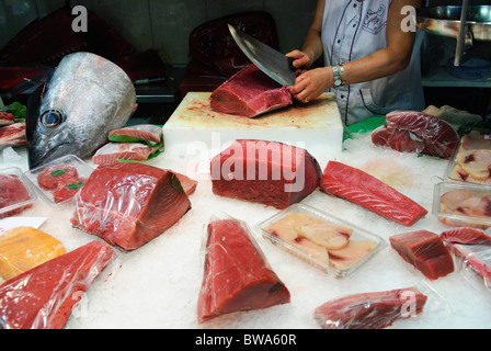 woman cuts a piece of fresh tuna fish with large knife at stall in La Boqueria market hall in Barcelona, Spain Stock Photo