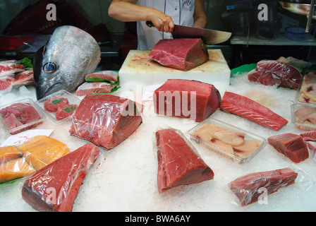 woman cuts a piece of fresh tuna fish with large knife at stall in La Boqueria market hall in Barcelona, Spain Stock Photo