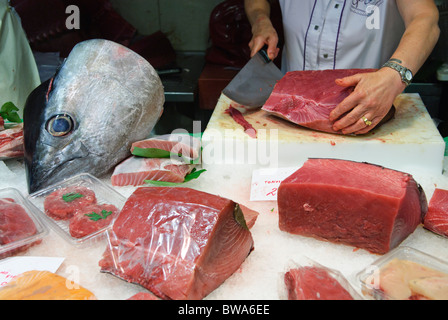 woman cuts a piece of fresh tuna fish with large knife at stall in La Boqueria market hall in Barcelona, Spain Stock Photo