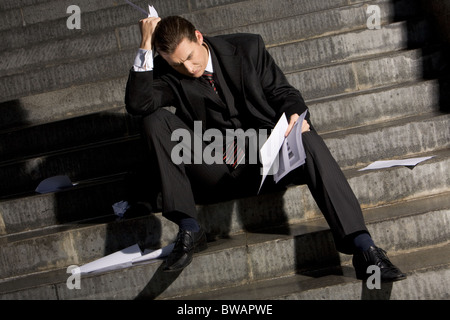 Photo of sad man with papers in hands sitting on stairs with no idea what to do Stock Photo