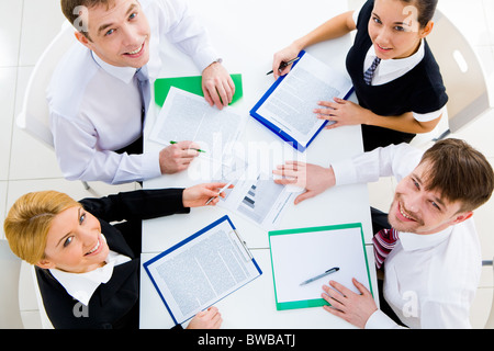 Several white collar workers looking upwards at camera from their workplace Stock Photo