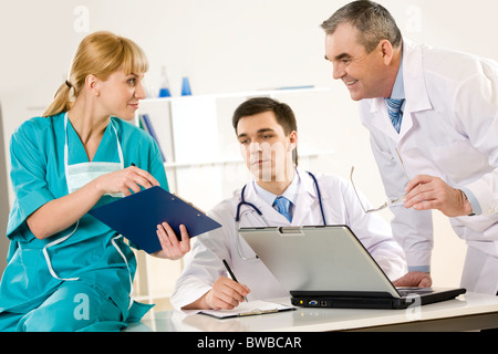 Photo of aged physician and young clinician looking at document in nurse’s hand Stock Photo
