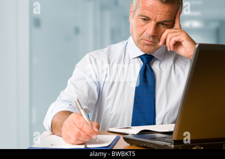 Absorbed mature businessman working and taking notes in his modern office Stock Photo