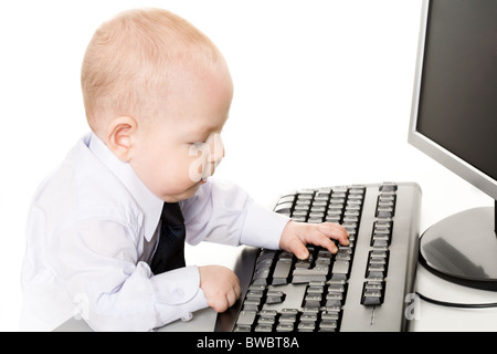 Photo of cute baby typing on keyboard with monitor in front of him Stock Photo