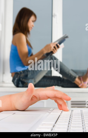 Close-up of child’s finger pushing keyboard button with reading woman at background Stock Photo