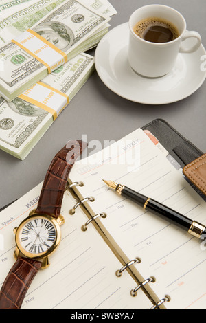 Image of open notepad with fountain pen and watch on it with cup of coffee and dollar banknotes near by Stock Photo