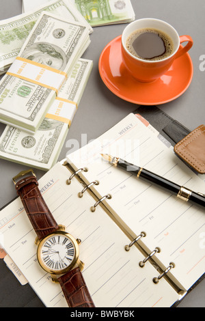 Image of open notepad with fountain pen and watch on it and red cup of coffee with dollar banknotes near by Stock Photo