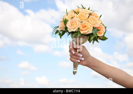 Close-up of bridal hand holding yellow rose bouquet on background of sky