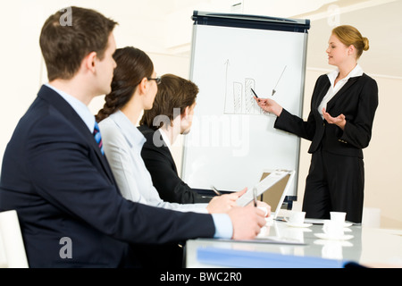 Photo of serious business people listening to female manager pointing at whiteboard while presenting new project Stock Photo