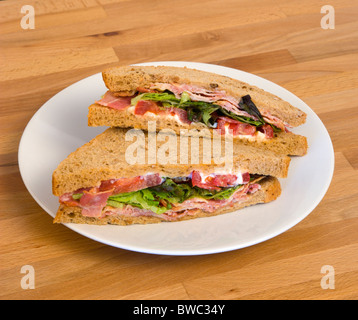 Food, Meal, Snack, Bacon lettuce and tomato BLT brown bread sandwich on a white plate on a wooden table top. Stock Photo