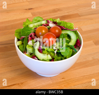 Food, Vegetables, Salad, White bowl of mixed green leaf salad with tomatoes and cucumber on a wooden table top. Stock Photo