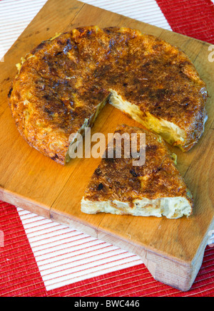 Food, Cooked, Eggs, Spanish omelette or tortilla on a wooden chopping board with a slice cut out. Stock Photo