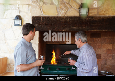 Two men by barbeque holding wine glasses Stock Photo