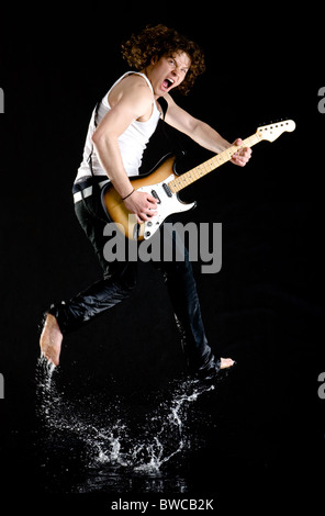 Portrait of dynamic performer with electrical guitar jumping and splashing water Stock Photo