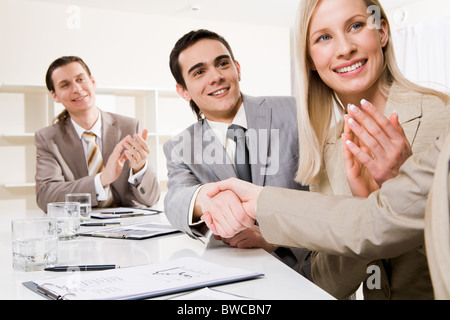 Photo of successful business partners handshaking after striking deal while their colleagues applauding Stock Photo