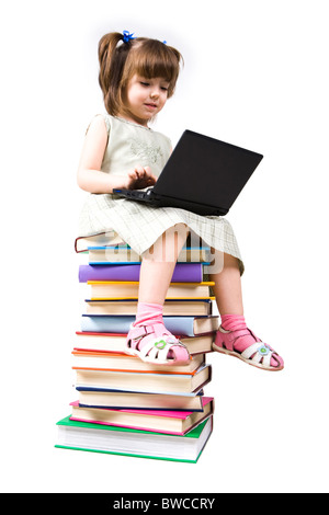 Portrait of clever girl sitting on books with laptop in front and typing Stock Photo