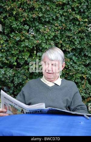 OAP man sitting outdoors reading a newspaper Stock Photo