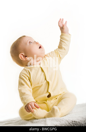 Portrait of adorable baby sitting with his arm raised and looking upwards Stock Photo