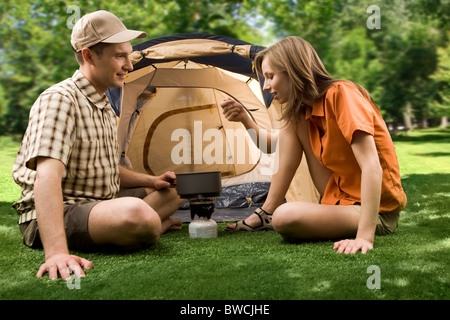 Photo of cheerful girl holding cup while her boyfriend pouring tea into it in the park Stock Photo