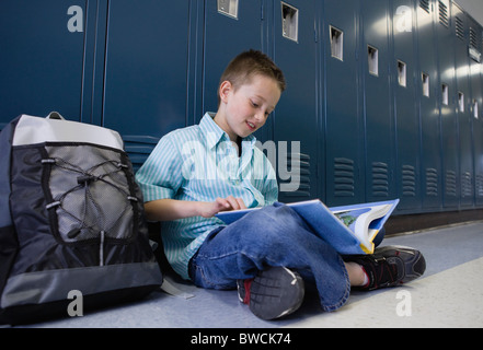 USA, Illinois, Metamora, Boy (8-9) sitting at lockers in school corridor and reading book Stock Photo