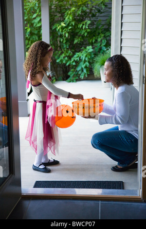 USA, Illinois, Metamora, Young woman giving candies to girl (6-7) in costume during Halloween Stock Photo