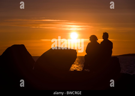 People sitting and enjoying the midnight sun setting over the Atlantic Ocean. Reykjavik Iceland. Stock Photo