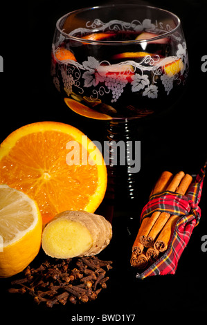 Traditional mulled wine in a green stemmed German glass surrounded by the ingredients: orange, lemon, cinnamon, cloves, ginger. Stock Photo