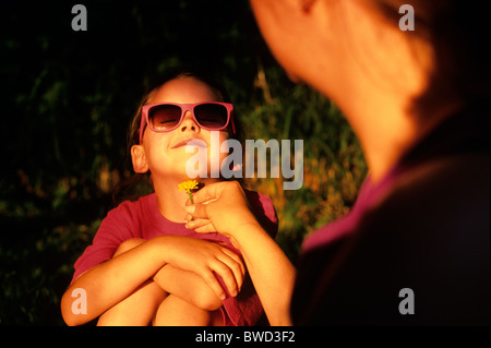 Young girl ( 6 years old) with dandelion put under her chin smiling summer game with mom ' Likes Butter' Stock Photo