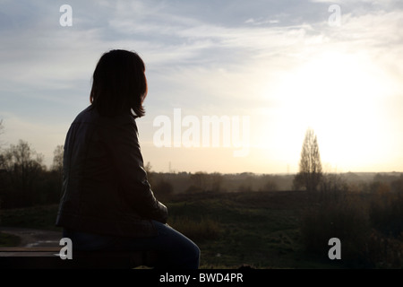 Silhouetted woman sitting alone watching the sun set, back view Stock Photo