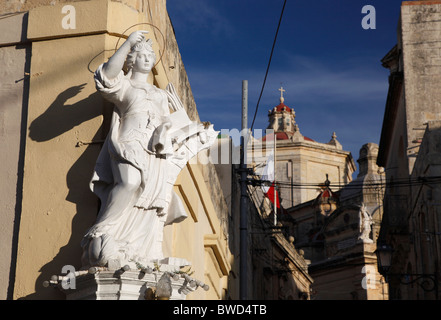 An old statue of the medieval saint St Catherine of Alexandria and the dome of the parish church in Zurrieq in Malta. Stock Photo