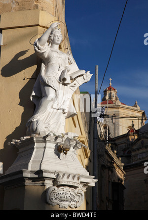 An old statue of the medieval saint St Catherine of Alexandria and the dome of the parish church in Zurrieq in Malta. Stock Photo