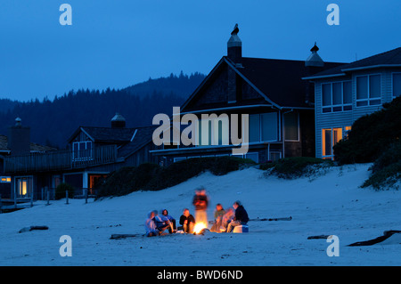 group of people sitting sit round a fire on cannon beach pacific ocean northwest oregon sunset dusk after dark night nighttime Stock Photo