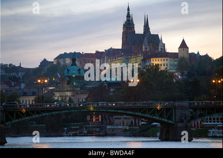 Prague castle and St Vitus Cathedral at dusk seen from river with bridge and traffic foreground Stock Photo