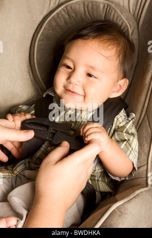 Smiling biracial Asian Filipino kid sitting in car seat while parent hands buckle him up Stock Photo