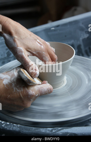 Hand of a female potter throwing a porcelain pot on a wheel and using a wooden scraper for shaping and trimming her pot Stock Photo