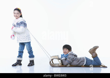 girl pulling the sled and boy laying on stomach Stock Photo