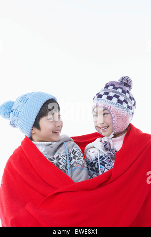 boy and girl covering red blanket with themselves Stock Photo