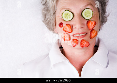 Face of mature woman with cucumber and strawberry slices on it Stock Photo