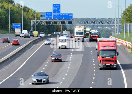 Gantry signs above M25 Motorway at Junction 27 for M11 routes with concrete crash barrier good traffic clockwise flow four lanes Essex England UK Stock Photo