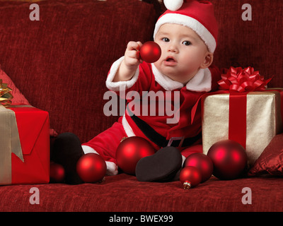 License available at MaximImages.com - Six month old baby boy wearing Santa Christmas costume and holding a red bauble in his hand Stock Photo