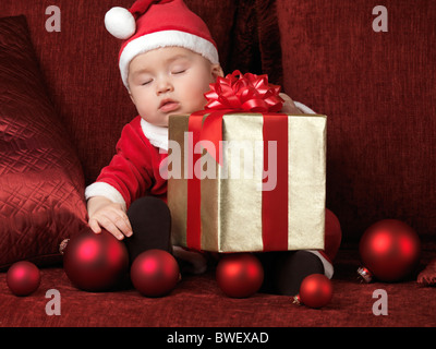 Six month old baby boy in Santa costume sleeping with a Christmas present in his lap Stock Photo