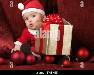 Six month old baby boy in Santa costume with a Christmas present on his lap Stock Photo