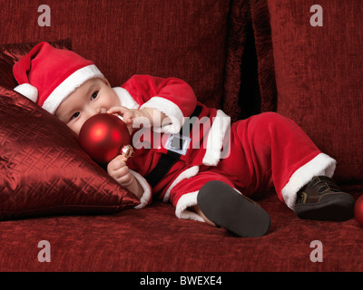License available at MaximImages.com - Six month old baby boy in Santa Christmas costume holding a red bauble in his hand Stock Photo