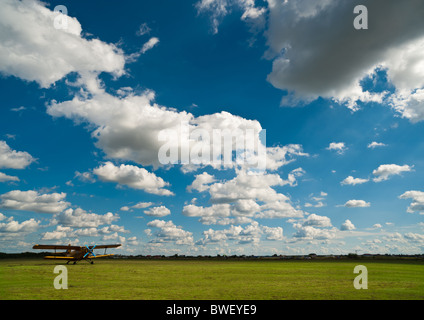 Yellow airplane on green airfield under blue sky with white clouds Stock Photo