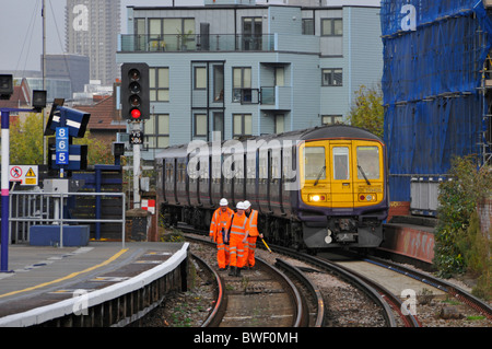 Railway infrastructure maintenance crew workers in high vis jackets & hard hat train running on third rail electric track South London England UK Stock Photo