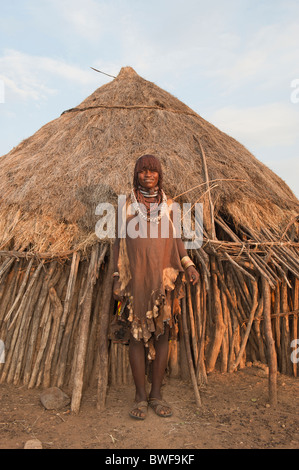 Pregnant Hamar woman with necklaces made of Cowry shells in front of her wooden hut, Omo river valley, Ethiopia Stock Photo